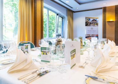 Festlich eingedeckter Tisch im Bankettsaal mit weißen Tischdecken, Gläsern, Menükarten und Kerzen – vorbereitet für ein gehobenes Event.