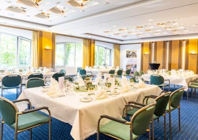 Veranstaltungsraum mit mehreren runden Tischen, Stühlen, Fensterfront und eleganter Beleuchtung – Raum für Feiern oder Tagungen.