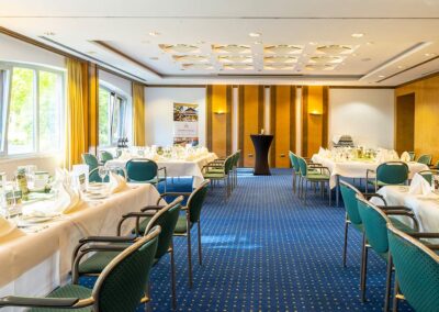 Veranstaltungsraum mit mehreren runden Tischen, Stühlen, Fensterfront und eleganter Beleuchtung – Raum für Feiern oder Tagungen.